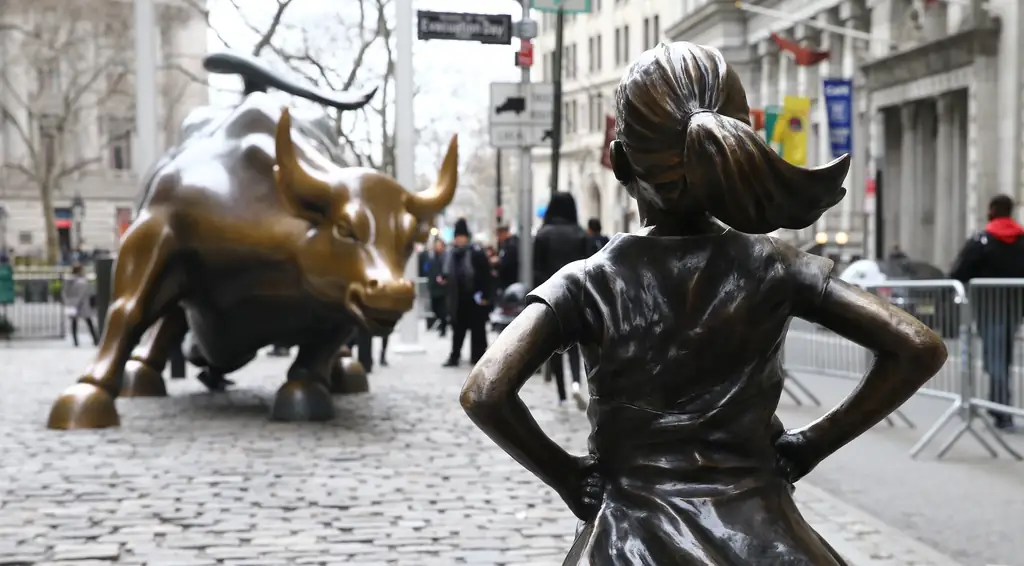 The Fearless Girl statue facing down Wall Street's Charging Bull, hands on her hips.